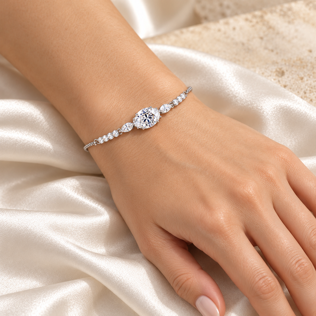 Celeste Oval Sparkle silver bracelet worn on model hand with ivory satin background